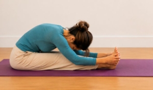 Femme en posture de flexion avant assise (paschimottanasana) sur un tapis de yoga mauve